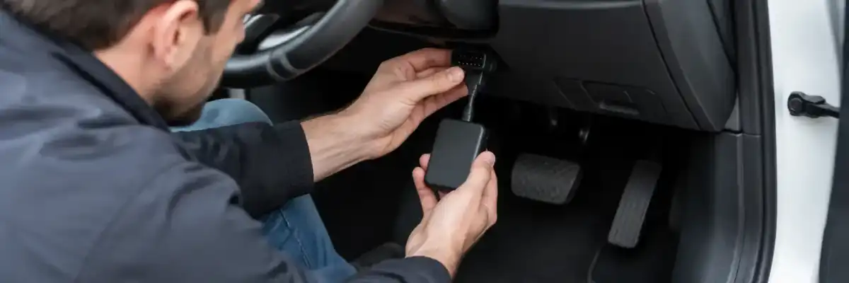 Driver connecting an unbranded telematics device beneath a car dashboard